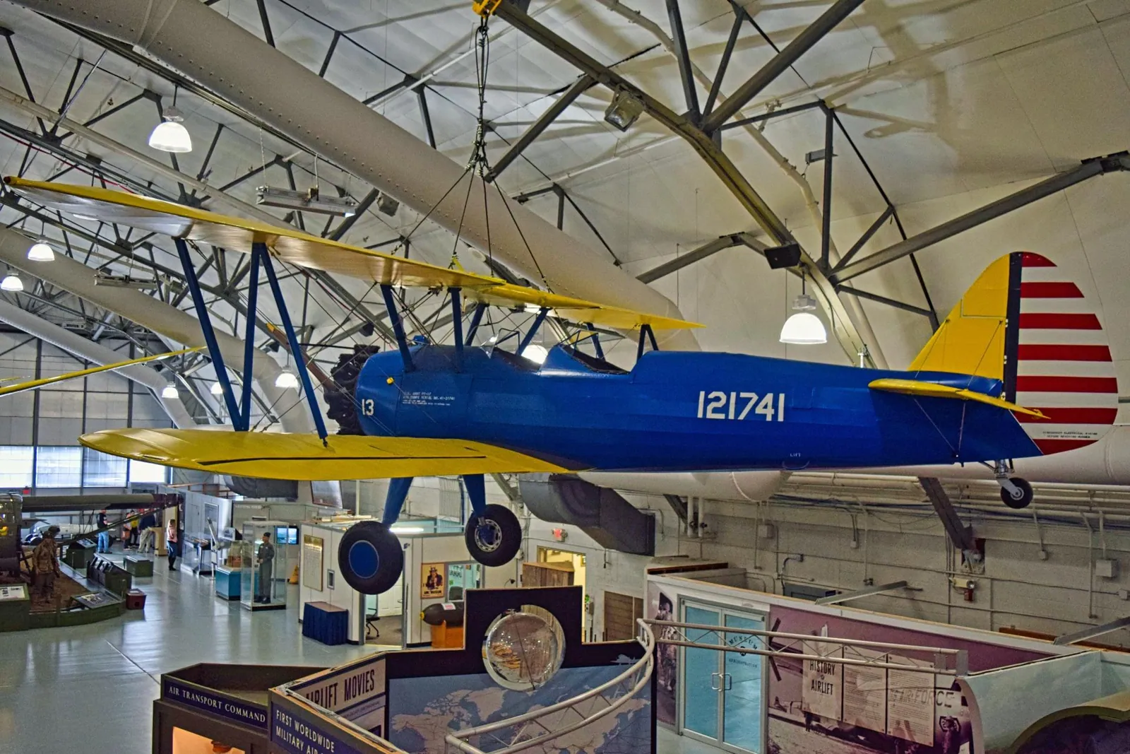 A blue and yellow Stearman biplane, tail number 121741, hanging in the Museum of Flight hangar