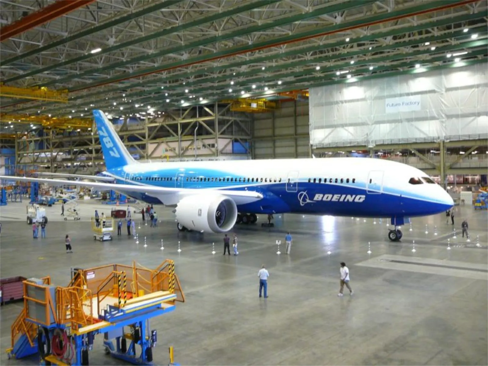 A Boeing 787 Dreamliner in Boeing house livery stands on the Everett factory floor, dwarfing the workers beside it