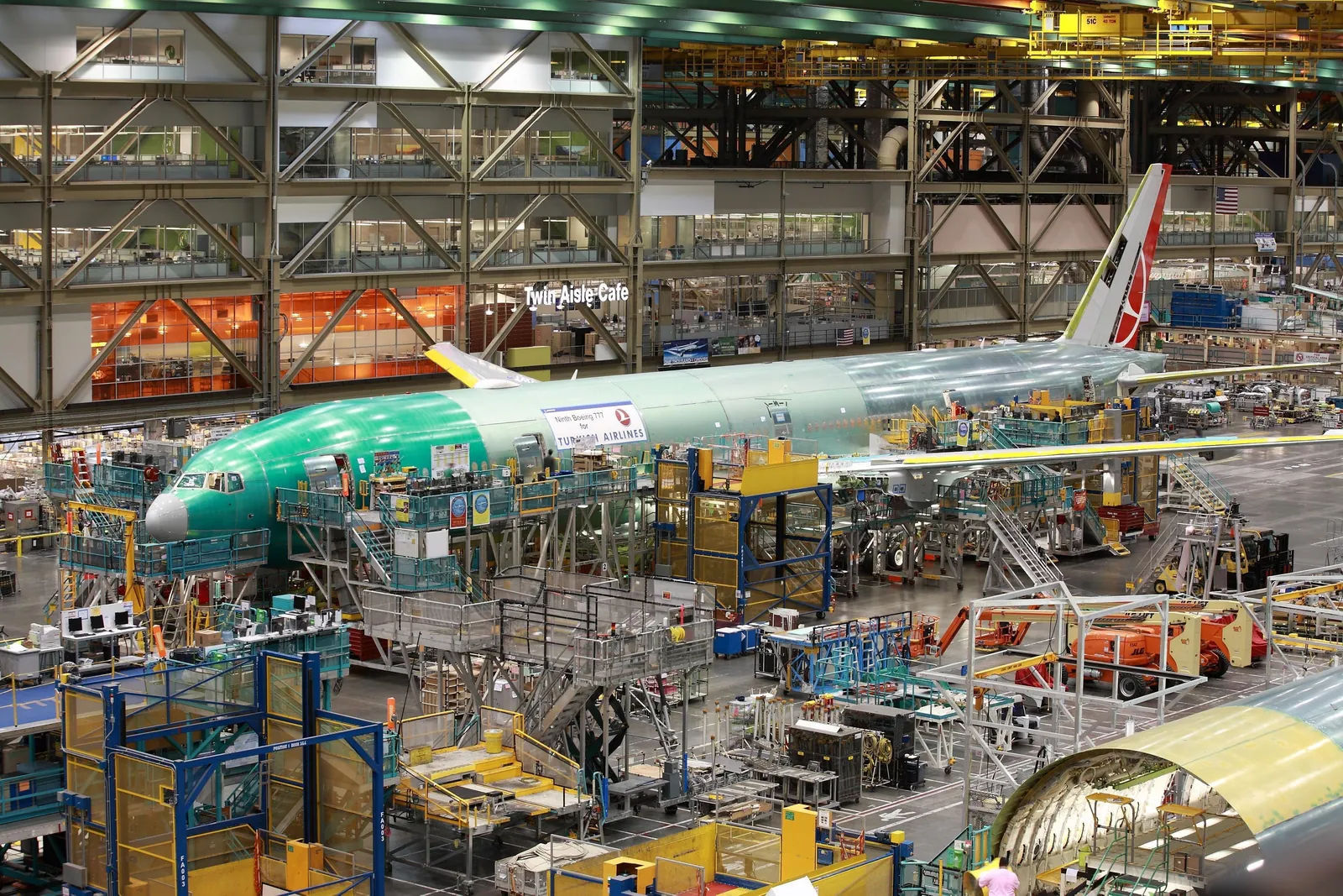 A widebody fuselage in green protective primer on the assembly line, seen from the visitor viewing level